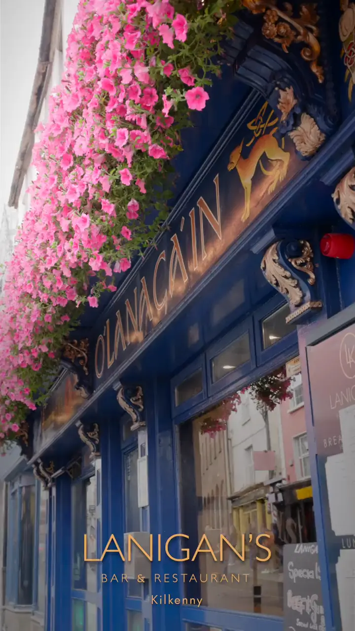 Pink flower display and gold lettering on the blue frontage of Lanigan's Bar, Rose Inn Street, Kilkenny